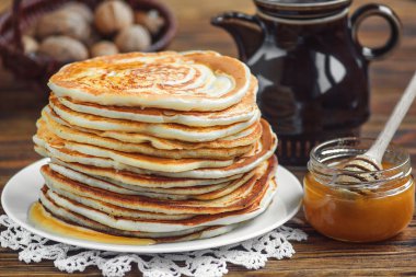 Ahşap arka plan üzerinde beyaz tabak üzerinde bal ile lezzetli, ev yapımı krep yığını. Sağlıklı kahvaltı, yakın çekim.