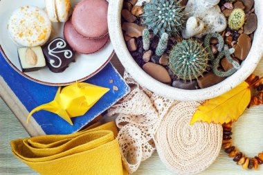 Colorful paper origami, colored macaroons, vintage lace ribbon, amber, flower in a pot, book and napkin on the table. Still life.