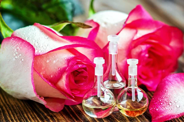 Ätherisches Öl in Glasflasche mit Rosenblüten auf Holzgrund. kleine Flaschen Parfüm. Schönheitsbehandlung. Wellness-Konzept. Selektiver Fokus. — Stockfoto