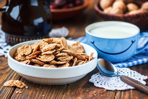 Céréales dans un bol en céramique blanche avec cuillère sur table en bois. Flocons multigrains et tasse de lait avec le sourire. Bonjour ou bonne journée concept de message. Petit déjeuner sain et concept de régime alimentaire, gros plan . — Photo