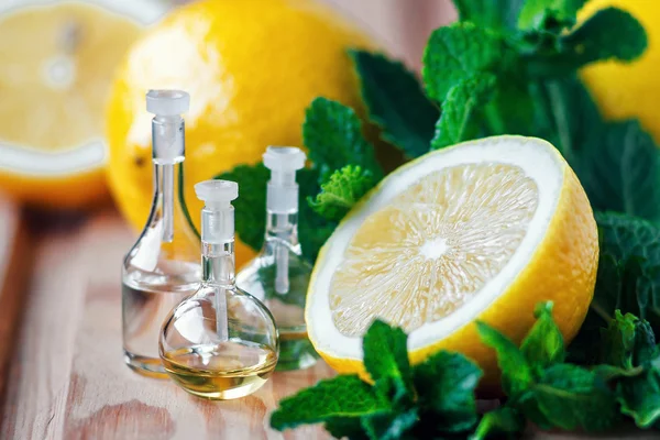 Aceite esencial en botella de vidrio con fruta fresca y jugosa de limón y hojas verdes de menta sobre fondo de madera. Tratamiento de belleza. Concepto Spa. Enfoque selectivo . — Foto de Stock