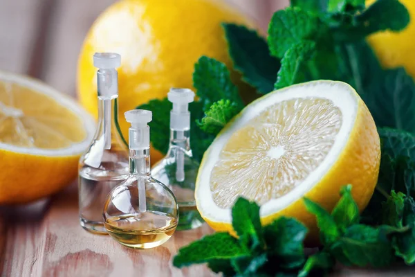 Essential oil in glass bottle with fresh, juicy lemon fruit and green leaves of mint-beauty treatment. Spa concept. Selective focus. — Stock Photo, Image