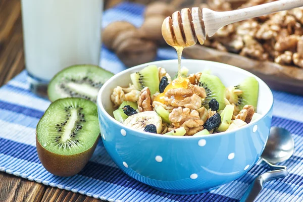 Biologische havermout PAP in keramische kom met bananen, honing, walnoten, Kiwi fruit en rozijnen. Gezond ontbijt-gezondheid en dieet concept op de houten tafel, close-up — Stockfoto