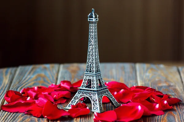 Wieża Eiffla pomnik i czerwone płatki róż na drewnianym tle. Podróże, koncepcja miłości. — Zdjęcie stockowe