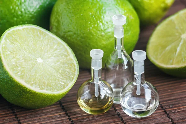 Essential oils in glass bottle with fresh, juicy, ripe limes. Beauty treatment. Spa concept. Selective focus. — Stock Photo, Image