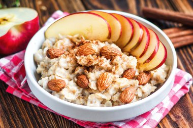 Elma, badem, bal ve tarçın ile beyaz seramik kase organik yulaf lapası. Sağlıklı kahvaltı - ahşap masada sağlık ve diyet konsepti, yakın.