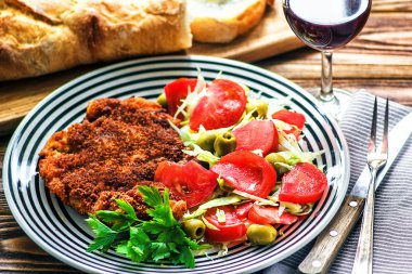 Ev yapımı Alman Weiner kotletpane Schnitzel ve domates, yeşil zeytin, marul ve maydanoz ahşap masa, closeup üzerinde beyaz kase taze sebze bahar salatası.