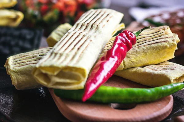 Breakfast two spicy delicious burritos mexican fast food dinner on wooden board wood table decorated with red and green hot peppers. Eggs pepper potatoes vegetables meat inside. Healthy lunch snack. — Stock Photo, Image