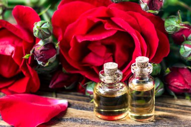 Kırmızı gül çiçek ve yaprakları ahşap arka plan üzerinde cam şişede esans. Güzellik bakımı. Spa ve aromaterapi kavramı. Seçici odak.