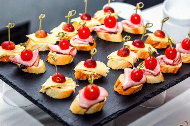 Izgara baget, kiraz domates, jambon dilimleri, peynir ve siyah arka plan üzerinde taze üzüm ile küçük crostini. Sandviçler veya çeşitli kanepeler karanlık bir tahta üzerinde, üst görünümü.