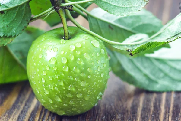 A ripe green apple with water droplets and leaves on the wooden table, macro in selective focus. — Stock Photo, Image