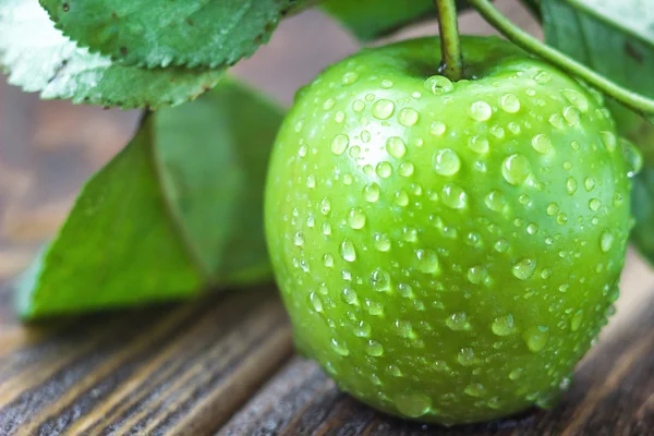 Una manzana verde madura con gotitas de agua y hojas en la mesa de madera, macro en enfoque selectivo . — Foto de Stock