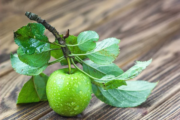 A ripe green apple with water droplets and leaves on the wooden table, macro in selective focus. — Stock Photo, Image