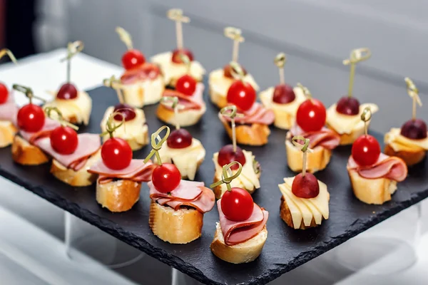 Izgara baget, kiraz domates, jambon dilimleri, peynir ve siyah arka plan üzerinde taze üzüm ile küçük crostini. Sandviçler veya çeşitli kanepeler karanlık bir tahta üzerinde, üst görünümü.