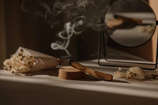  Palo Santo dumandan bir jet, ayna ve kurumuş çiçeklerle tarafsız bir arkaplanda. Soyut moda filmi. Minimalist wabi sabi tarzı.