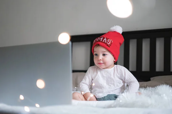 Baby baby met kerstmuts chatten via lap top thuis tijdens quarantaine. Sociale afstand tijdens de afsluiting. Nieuwjaar en kerstviering thuis — Stockfoto