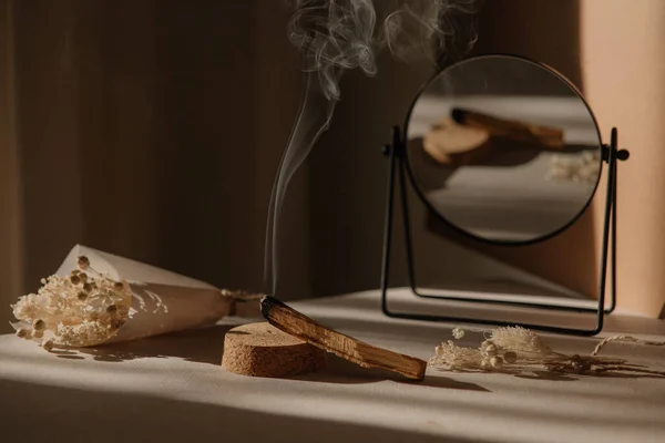  Palo Santo dumandan bir jet, ayna ve kurumuş çiçeklerle tarafsız bir arkaplanda. Soyut moda filmi. Minimalist wabi sabi tarzı.