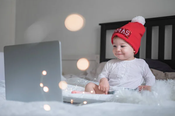 Baby baby met kerstmuts chatten via lap top thuis tijdens quarantaine. Sociale afstand tijdens de afsluiting. Nieuwjaar en kerstviering thuis — Stockfoto