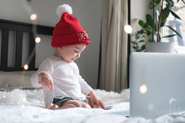 Baby baby met kerstmuts chatten via lap top thuis tijdens quarantaine. Sociale afstand tijdens de afsluiting. Nieuwjaar en kerstviering thuis — Stockfoto