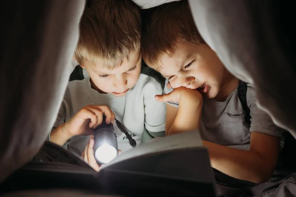 Deux petits frères lisant un livre la nuit se cachant sous la couverture — Photo