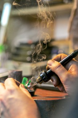 Adam mücevher atölyesinde yüzüğü elleriyle lehimliyor.