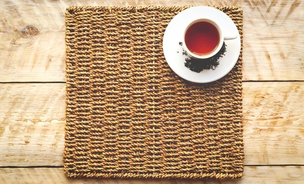 Taza de té sobre una alfombra de mimbre wodden fondo de tabla —  Fotos de Stock