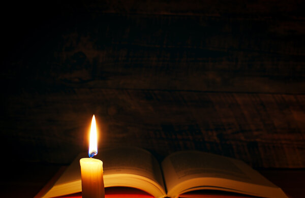 Concept of knowledge - vintage book with candle on wooden background