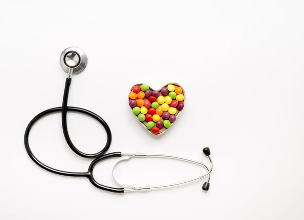 Estetoscópio em fundo branco com pílulas em forma de coração — Fotografia de Stock