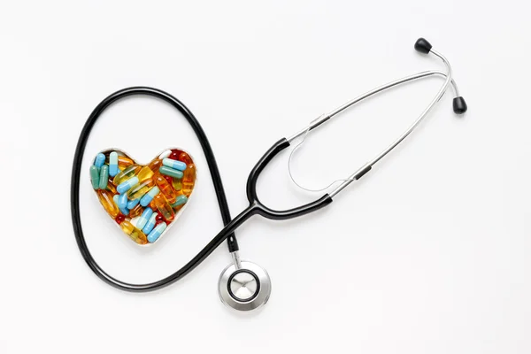 Estetoscópio em fundo branco com pílulas em forma de coração — Fotografia de Stock