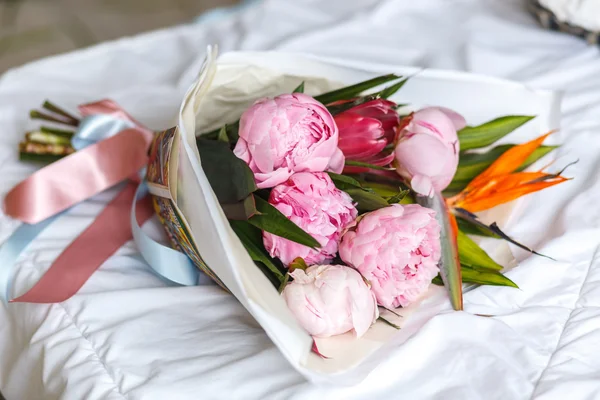 Bouquet of peonies in kraft paper on bed