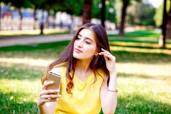 молодая девушка с телефоном в парке летом

