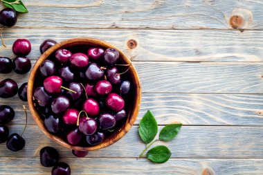 Tahta kasede yaprakları olan kırmızı kirazlar. Düzen, böğürtlen arka planı