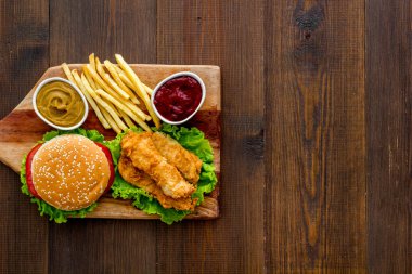 Klasik hamburger, ahşap kesim tahtasında patates kızartması ve kızarmış tavukla servis edilir.