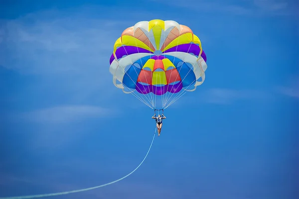 Young woman flying with colorful bright large parachute above th