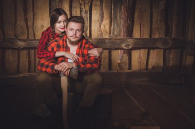 Stil oduncu. Oduncu bir sakal ve bıyık, ahşap bir arka plan üzerinde kırmızı bir gömlek, pantolon ve jartiyer ve kız arkadaşı giyiyor. Modern tarz. Seven beyaz çift tarzı oduncu