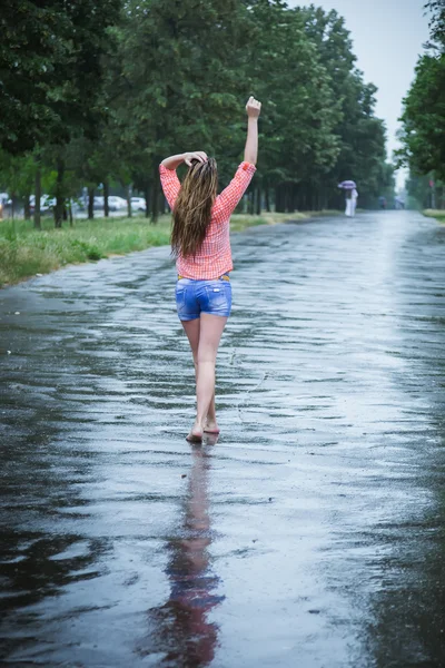 Jeune belle caucasienne blonde en short et chemise marchant dans le parc sous la pluie chaude estivale pieds nus à travers les flaques d'eau. Amusez-vous bien. Pluie tombante. Des gouttes de pluie. Vêtements humides, cheveux mouillés — Photo