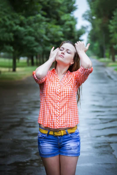 Jeune belle caucasienne blonde en short et chemise marchant dans le parc sous la pluie chaude estivale pieds nus à travers les flaques d'eau. Amusez-vous bien. Pluie tombante. Des gouttes de pluie. Vêtements humides, cheveux mouillés — Photo