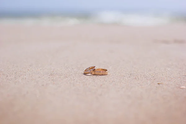 Dois anéis de casamento de ouro liso jazem na praia na areia — Fotografia de Stock