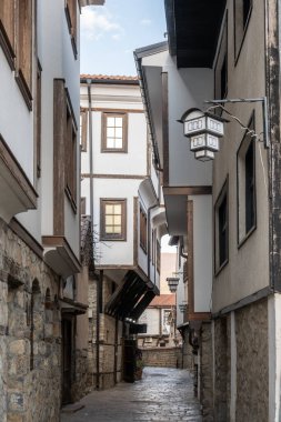 Dar, taştan döşenmiş bir ara sokak, Ohrids 'in tarihi kasabasından esiyor. Duvarları beyazlatılmış duvarlar, yüksek katlar, ahşap aksanlar ve karmaşık fener demirbaşlarıyla çevrili..