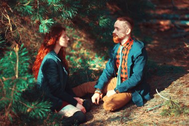 Kızıl saçlı adam, sakallı ve kıvırcık kızıl saçlı kız doğanın muhteşem manzarasının arka planında. Ormanda yürüyüşe çıkmış güzel bir çift..