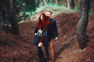 Kızıl saçlı adam, sakallı ve kıvırcık kızıl saçlı kız doğanın muhteşem manzarasının arka planında. Ormanda yürüyüşe çıkmış güzel bir çift..