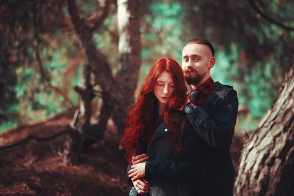 The red-haired guy with a beard and curly red-haired girl on the background of fabulous scenery of nature. Beautiful loving couple on a walk in the woods.