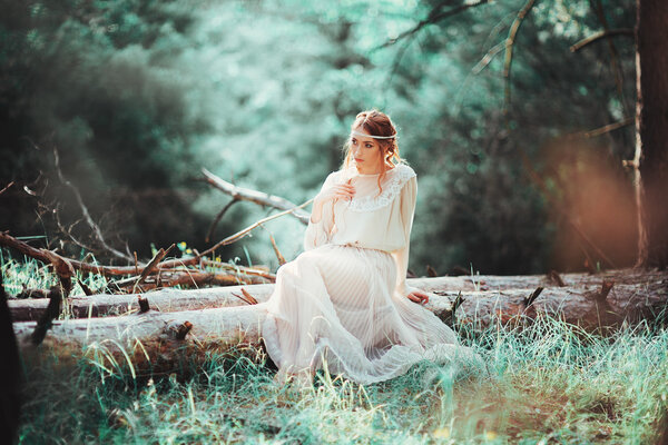 Beautiful artistic photo ginger girl in white dress sitting on a tree in the woods.