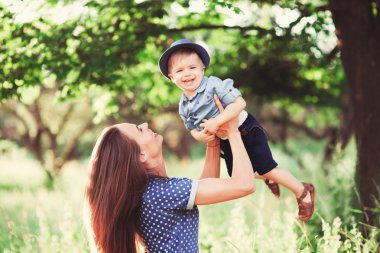 Sevgi dolu bir anne oğlunu kollarında tutuyor, onunla oynuyor ve ona sarılıyor. Aile doğada dinleniyor. yumuşak odak