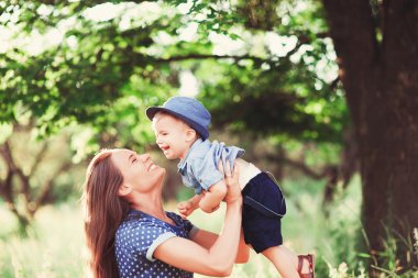 Sevgi dolu bir anne oğlunu kollarında tutuyor, onunla oynuyor ve ona sarılıyor. Aile doğada dinleniyor. yumuşak odak