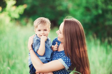 Sevgi dolu bir anne oğlunu kollarında tutuyor, onunla oynuyor ve ona sarılıyor. Aile doğada dinleniyor. yumuşak odak