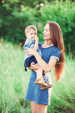 Sevgi dolu bir anne oğlunu kollarında tutuyor, onunla oynuyor ve ona sarılıyor. Aile doğada dinleniyor. yumuşak odak