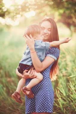 Sevgi dolu bir anne oğlunu kollarında tutuyor, onunla oynuyor ve ona sarılıyor. Aile doğada dinleniyor. yumuşak odak