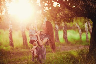 Sevgi dolu bir anne oğlunu kollarında tutuyor, onunla oynuyor ve ona sarılıyor. Aile doğada dinleniyor. yumuşak odak