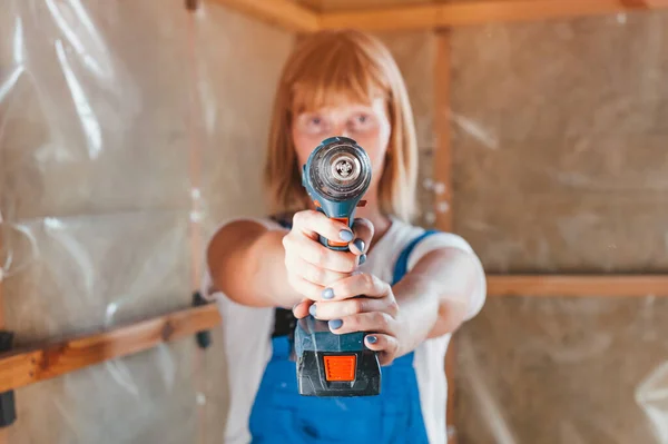 Woman builder in work overalls with drill and nail gun